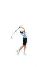 Junior golfer in a patterned polo and black shorts at the top of his backswing, cut out on white
