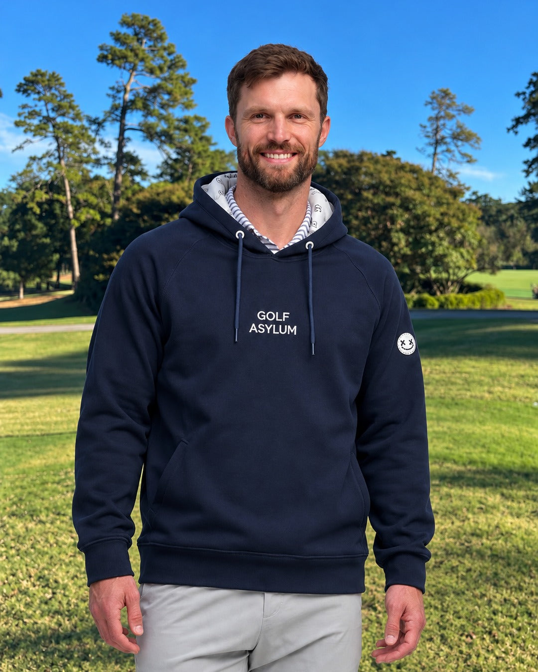Navy adult Golf Asylum hoodie worn on the course, with the wordmark on the chest, a Ballhead sleeve patch and a printed hood lining